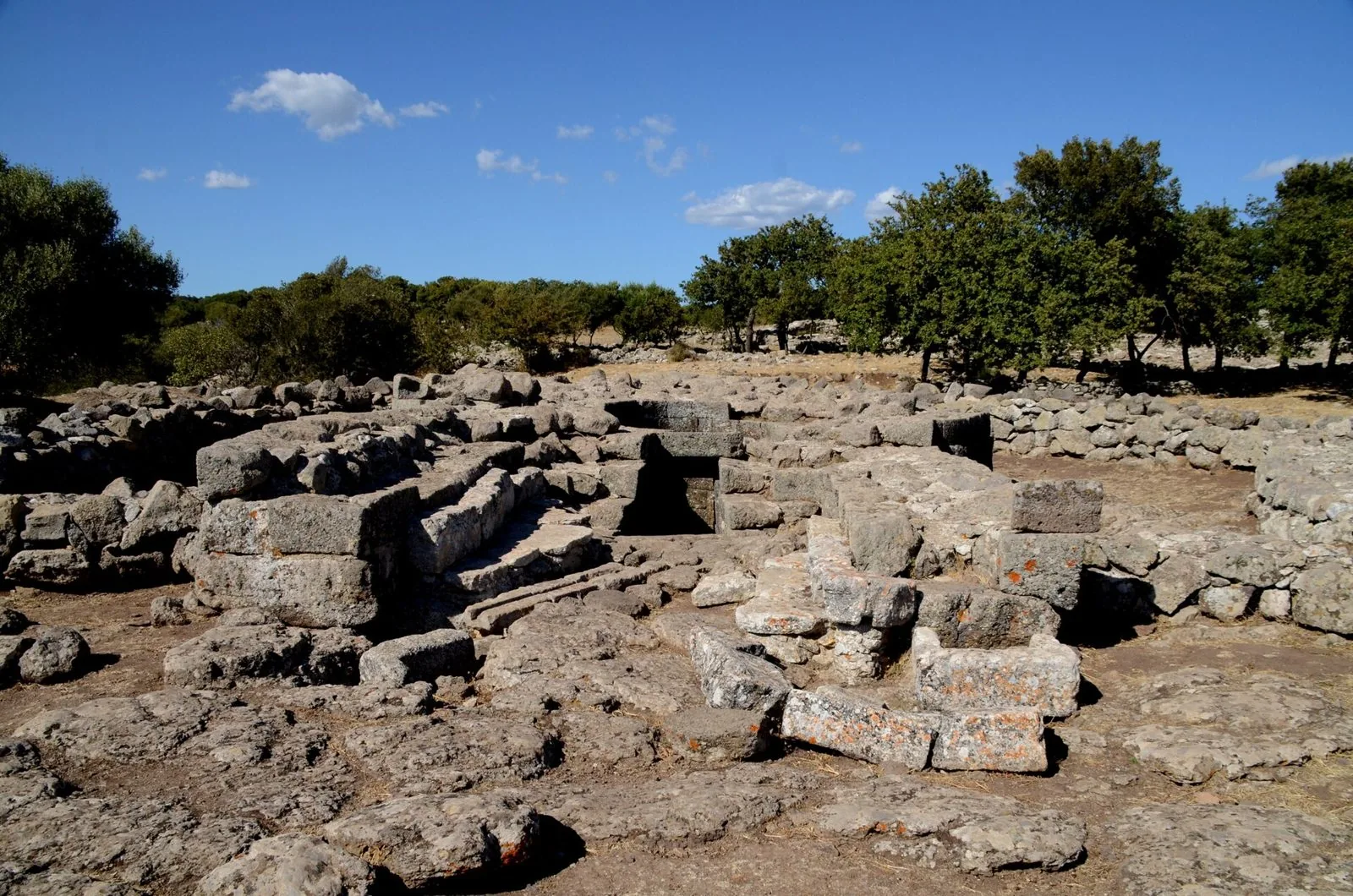 Resti in blocchi di pietra del tempio a pozzo nel santuario nuragico di Santa Vittoria di Serri, con la scalinata d'accesso e alberi sullo sfondo