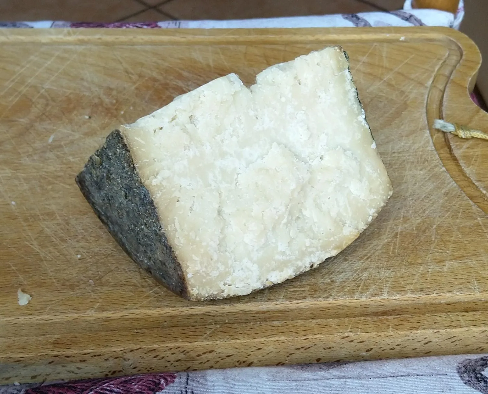 Una fetta di pecorino Fiore Sardo con la crosta scura e la pasta chiara e granulosa, appoggiata su un tagliere di legno