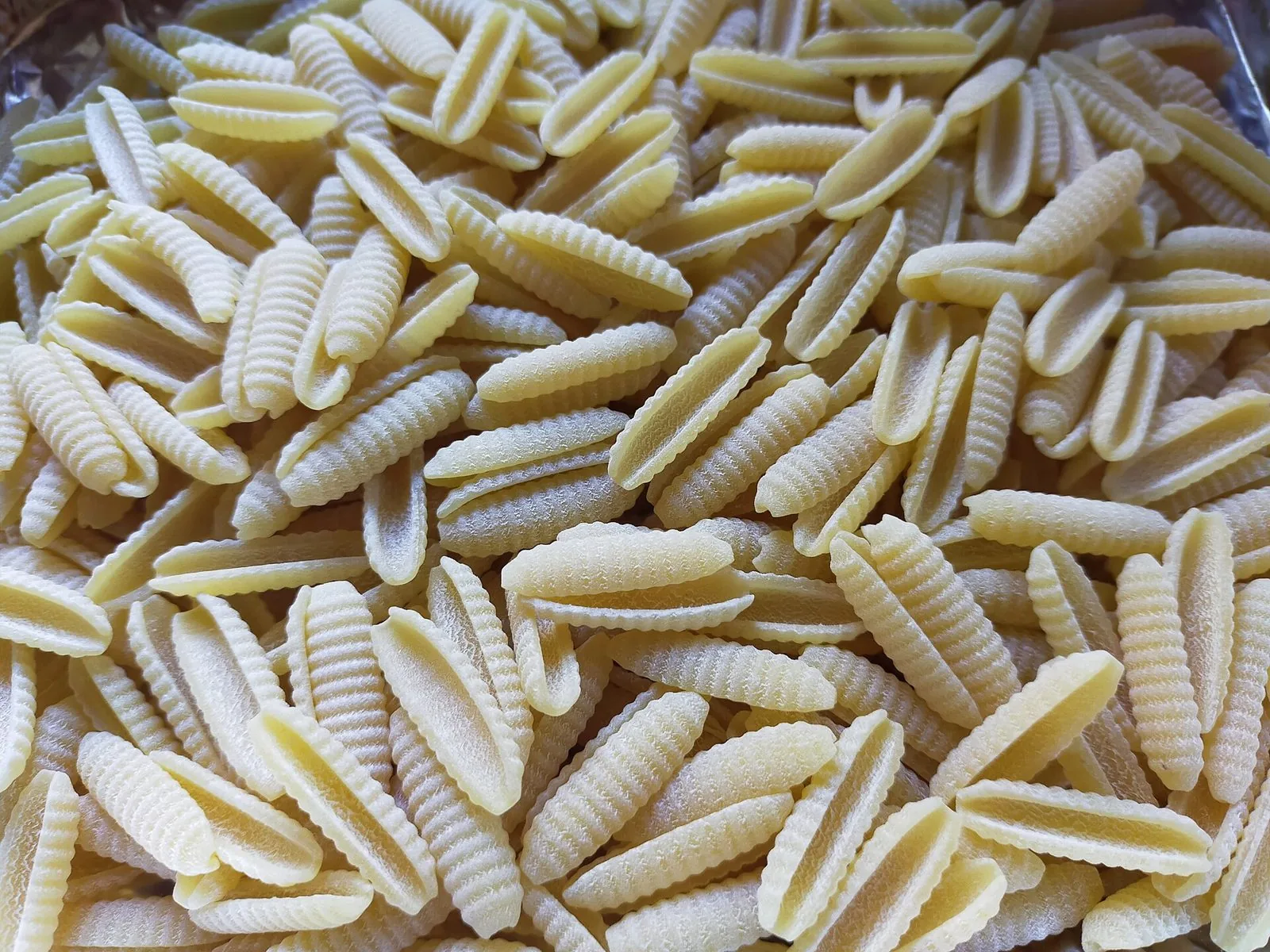 Primo piano di malloreddus crudi, piccoli gnocchetti di semola rigati color paglierino ammucchiati su un vassoio